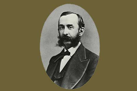 Oval framed black and white portrait of man with dark hair, mustache, and mutton chops