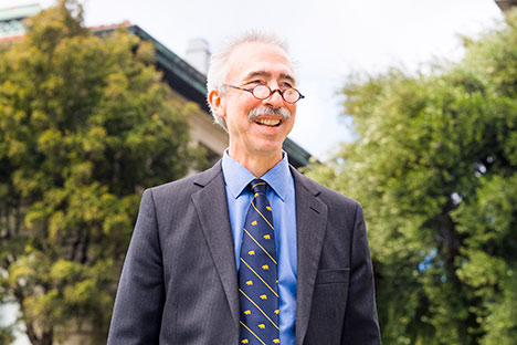 Smiling man wearing blue suit and tie, glasses with building in background