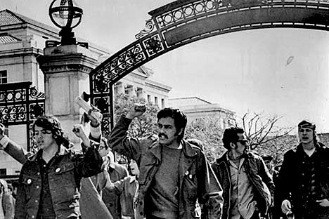 People marking through Sather Gate with their fists in the air.