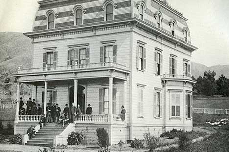 Black and white photo of large dwelling and group of people standing on the veranda