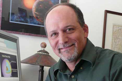 Man with beard and mustache sitting in front of framed image of planets