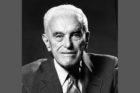 White haired man with suit and tie looking back at viewer