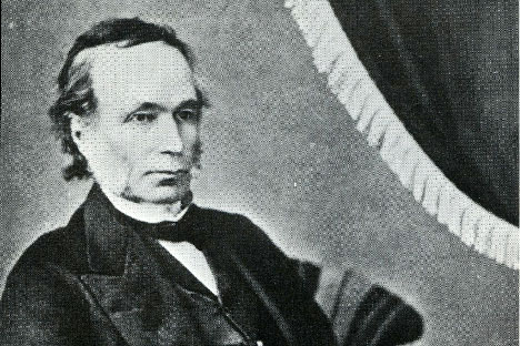 Black and white rendering of man sitting at an angle with drapery in background