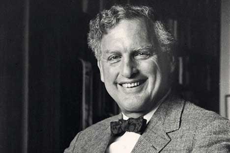 Man with wavy hair wearing suit and bowtie broadly smiling