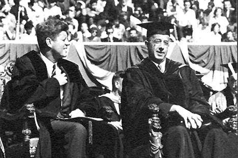 Black and white photo of John F. Kennedy sitting next to Clark Kerr in academic robes
