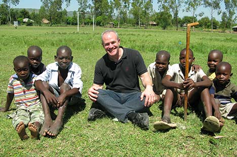 White male sitting on grass with seven young black boys