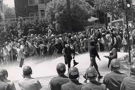 Water spraying on protesters as crowds and National Guard troops look on.