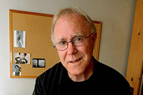 Blonde haired man wearing wire-rimmed glasses with bulletin board in background