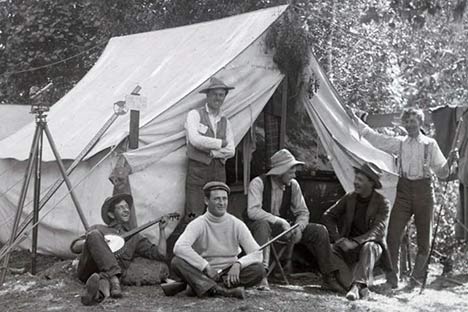 Six men in front of a tent. One of them is playing a banjo.