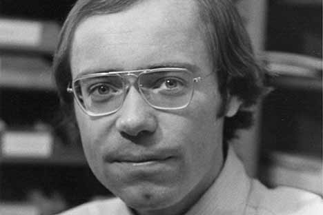 Young male wearing wire-rimmed glasses looking back at viewer