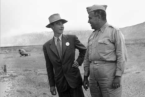 Two men standing in desert. One is wearing a suit and the other is wearing military apparel.