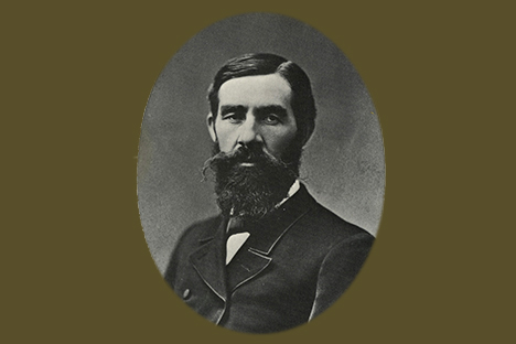 Oval framed black and white portrait of a bearded and mustachioed man with dark hair