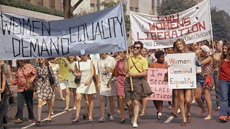 Women marching while holding banners that read 'Women demand equality'
